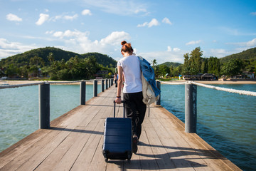 Girl tourist dragging luggage on a dock to tropical beach