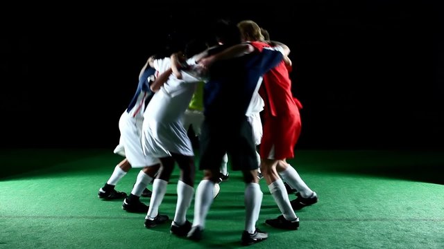 A group of soccer players huddle in a circle and jump together in unison 