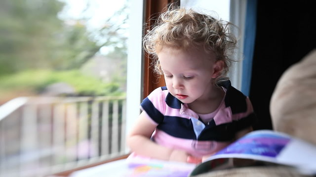 An adorable girl turns the pages of her picture book