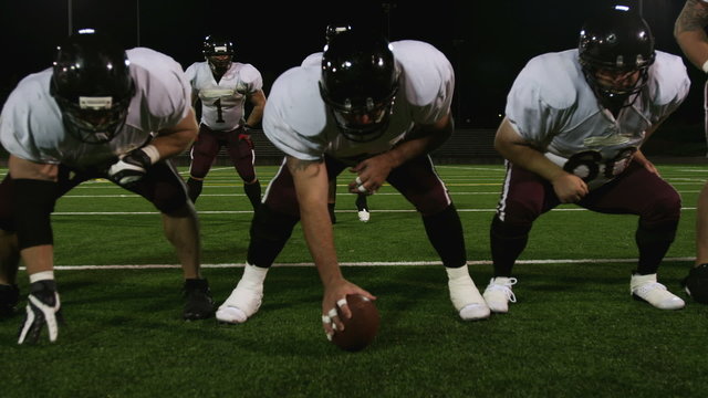 A football team sets up at the line of scrimmage and hikes the ball