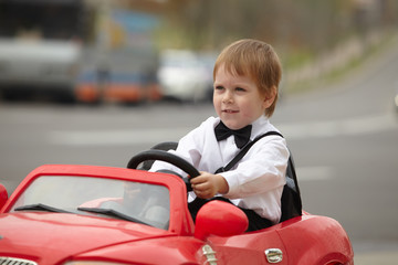 year-old boy in a white shirt in a red toy car in the street
