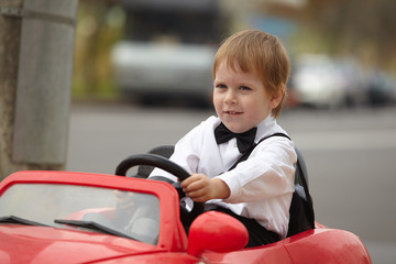 year-old boy in a white shirt in a red toy car in the street