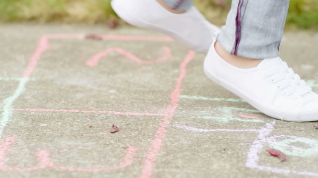 Slow motion tracking shot of a pair of feet jumping while playing hopscotch
