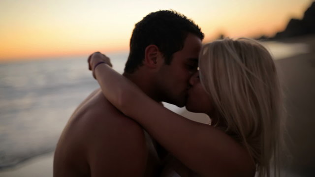 A cute couple kisses on the beach while the sun sets