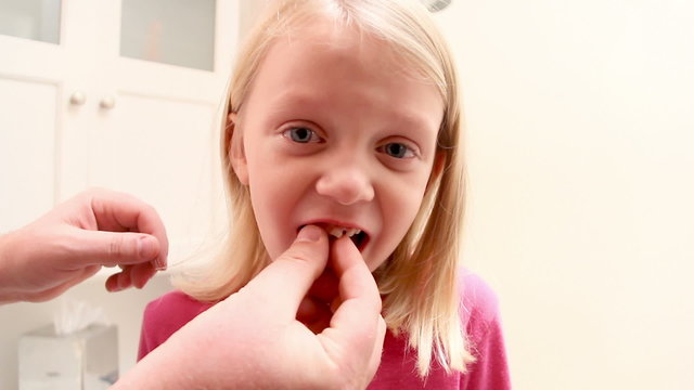 Father helps his daughter with her loose tooth by trying to loosen in up