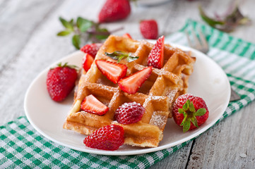 Belgium waffles with strawberries and mint on white plate