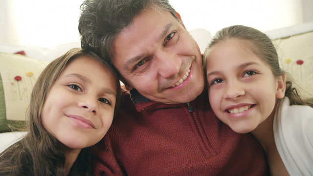 Two girls sit next to their dad as they all three smile for the camera