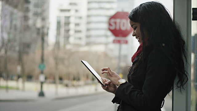 A young woman plays with her tablet as she wait for her bus