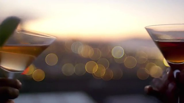 Close up of two cocktail glasses toasting on rooftop at dusk