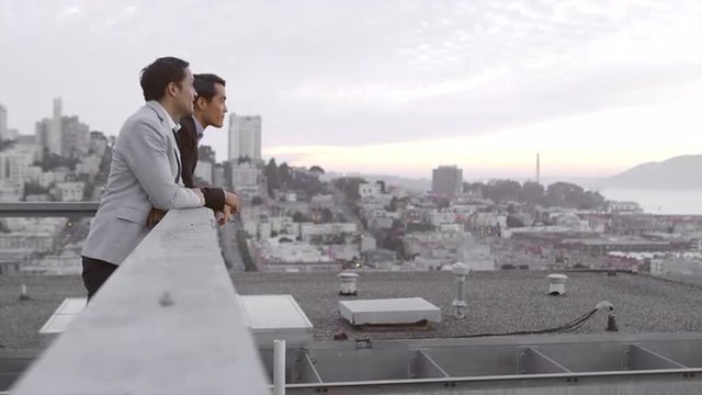 Two guys just hanging out on a roof and looking out to San Francisco bay during the day