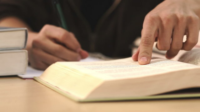 Close up of a student taking notes while reading a textbook