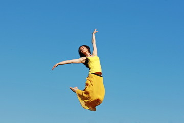 девушка в прыжке на фоне неба в желтом платье 