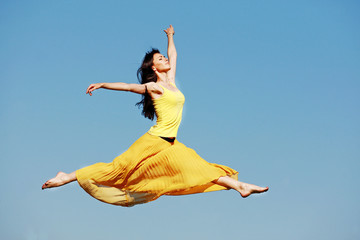 девушка в прыжке на фоне неба в желтом платье  - obrazy, fototapety, plakaty
