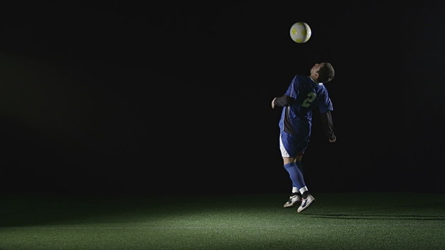 A soccer player catches a ball with his chest and then jumps and kicks the ball