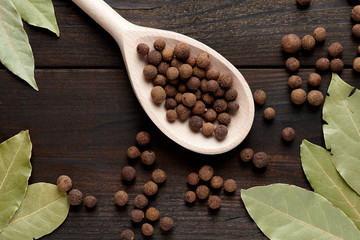 allspice on a wooden spoon surrounded by a bay leaf and allspice