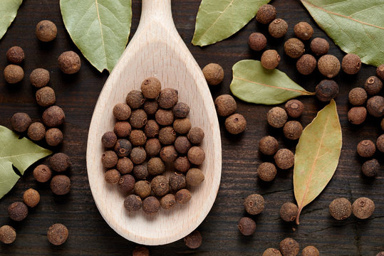 allspice on a wooden spoon surrounded by a bay leaf and allspice
