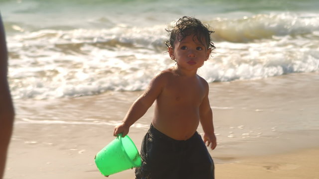 A young boy plays with buckets while at the beach