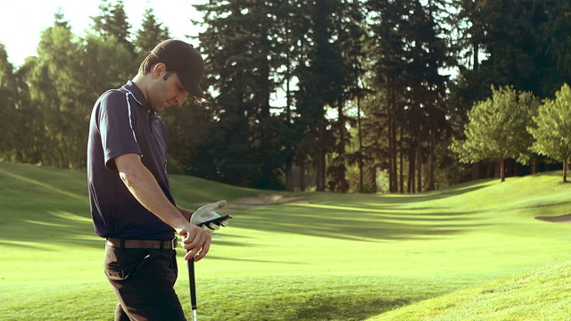 A golfer stands with his club looking at his phone and texting with it