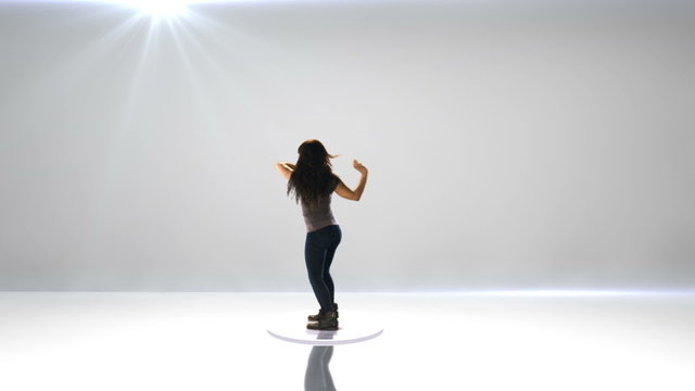 A young woman dances on a spinning turn table on a gray background