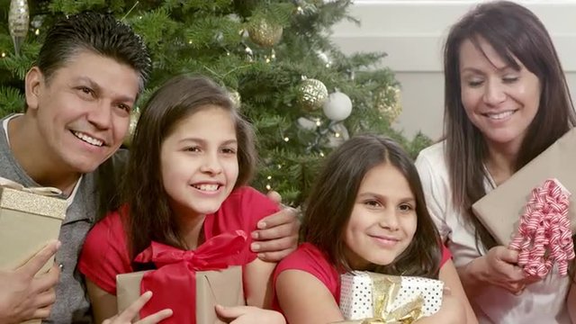 A family sitting under their christmas tree holds their presents and pose for a picture