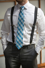 Young man wearing suspenders and colorful tie with hands in pock