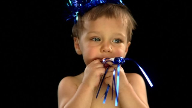 A white baby boy wears a party hat and blows a noise maker
