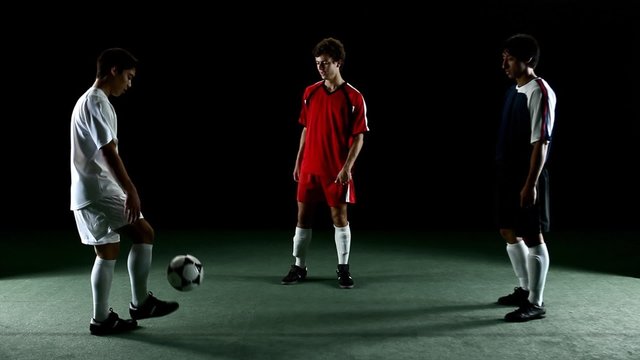 Three soccer players stand in a circle and kick the ball to each other 
