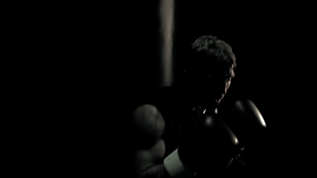 Boxer works on his form by training on a punching bag. Medium shot.