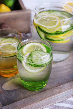 Fresh water with lemon and cucumber in glassware in wooden tray, closeup