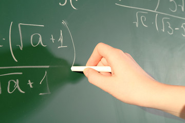 Teacher hand writing formulas on blackboard background