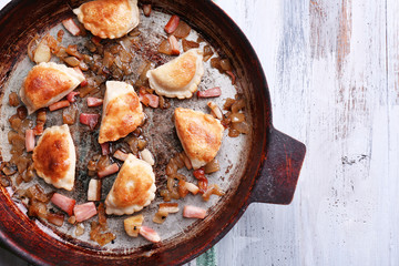 Fried dumplings with onion and bacon in frying pan, on wooden table background