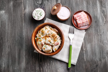 Fried dumplings with onion and bacon in frying pan, on wooden table background