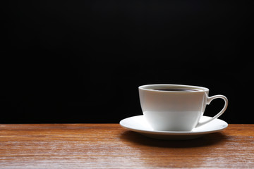 Cup of coffee on wooden table on black background