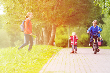 happy mother with two kids on scooter and bike in the park