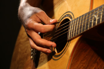 Young man playing on acoustic guitar close up