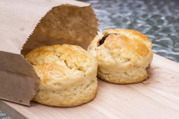 Scone on wooden plate and paper bag.