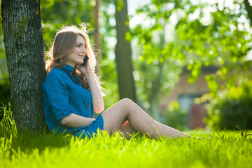 Naklejka na ściany i meble Pretty young caucasian woman sitting outside under a tree