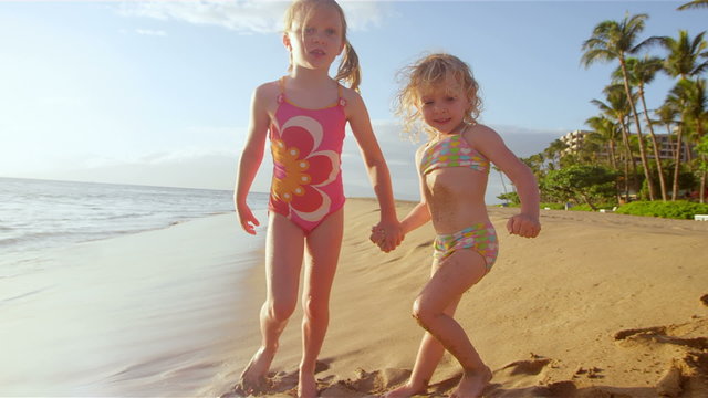 Two little girls hold hands and strut their stuff while walking down a beach