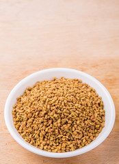 Fenugreek seeds in white bowl on wooden surface
