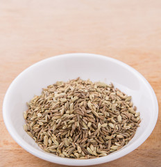 Cumin seed spice in white bowl on wooden surface