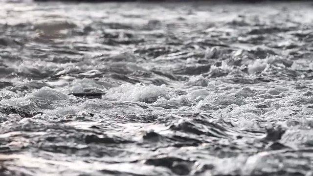 Close up abstract view of rushing water flowing down the river in winter, in slow motion