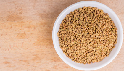 Fenugreek seeds in white bowl on wooden surface