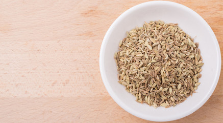 Cumin seed spice in white bowl on wooden surface