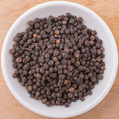 Black pepper in white bowl on wooden surface