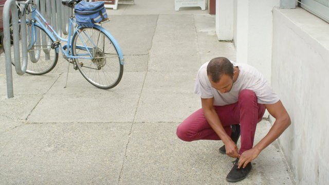 A man stops walking down the street in order to bend over and tie his shoelace