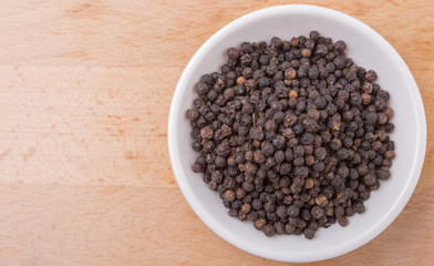 Black pepper in white bowl on wooden surface