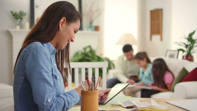 A mother goes over bills and looks worried as her family sits behind her
