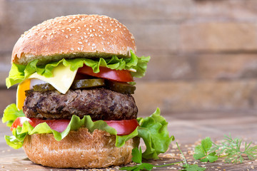 Big hamburger with beef cutlet and vegetables on wood background
