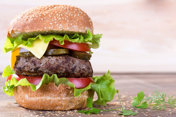Big hamburger with beef cutlet and vegetables on wood background