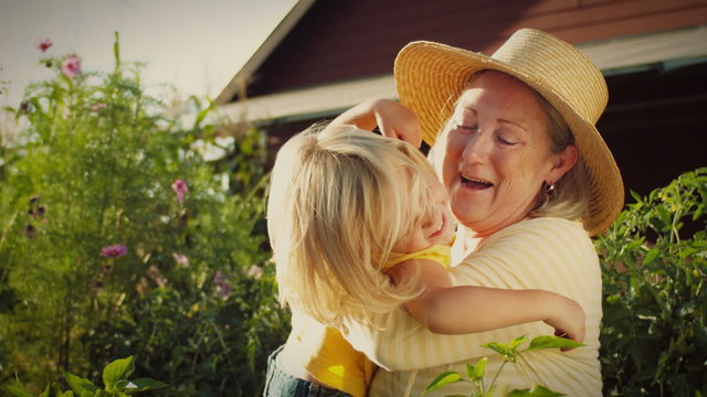 A little blonde girl runs to her grandmother's arms in a garden